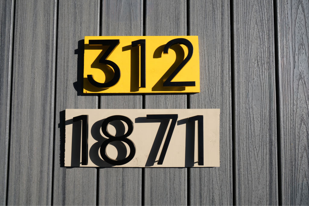 An Adoorn Address Numbers studied display showing 4-inch Mailbox Numbers and 6-inch House Numbers in matte black and brushed aluminum together on a styled card.