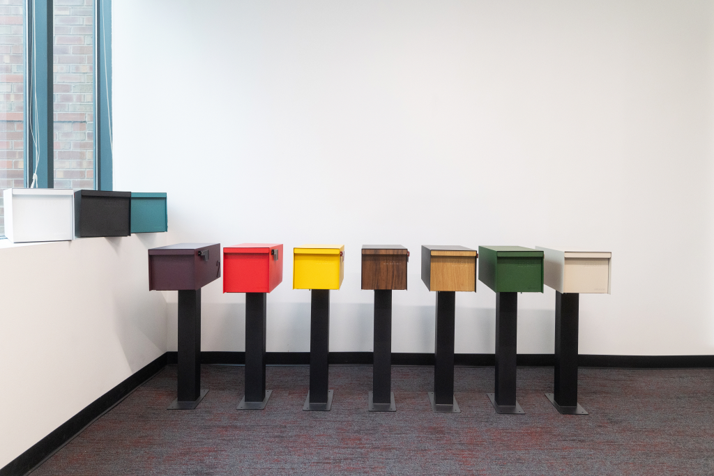 A row of Adoorn post mount mailboxes in mid-century black, color, and wood-grain finishes, shown side by side.