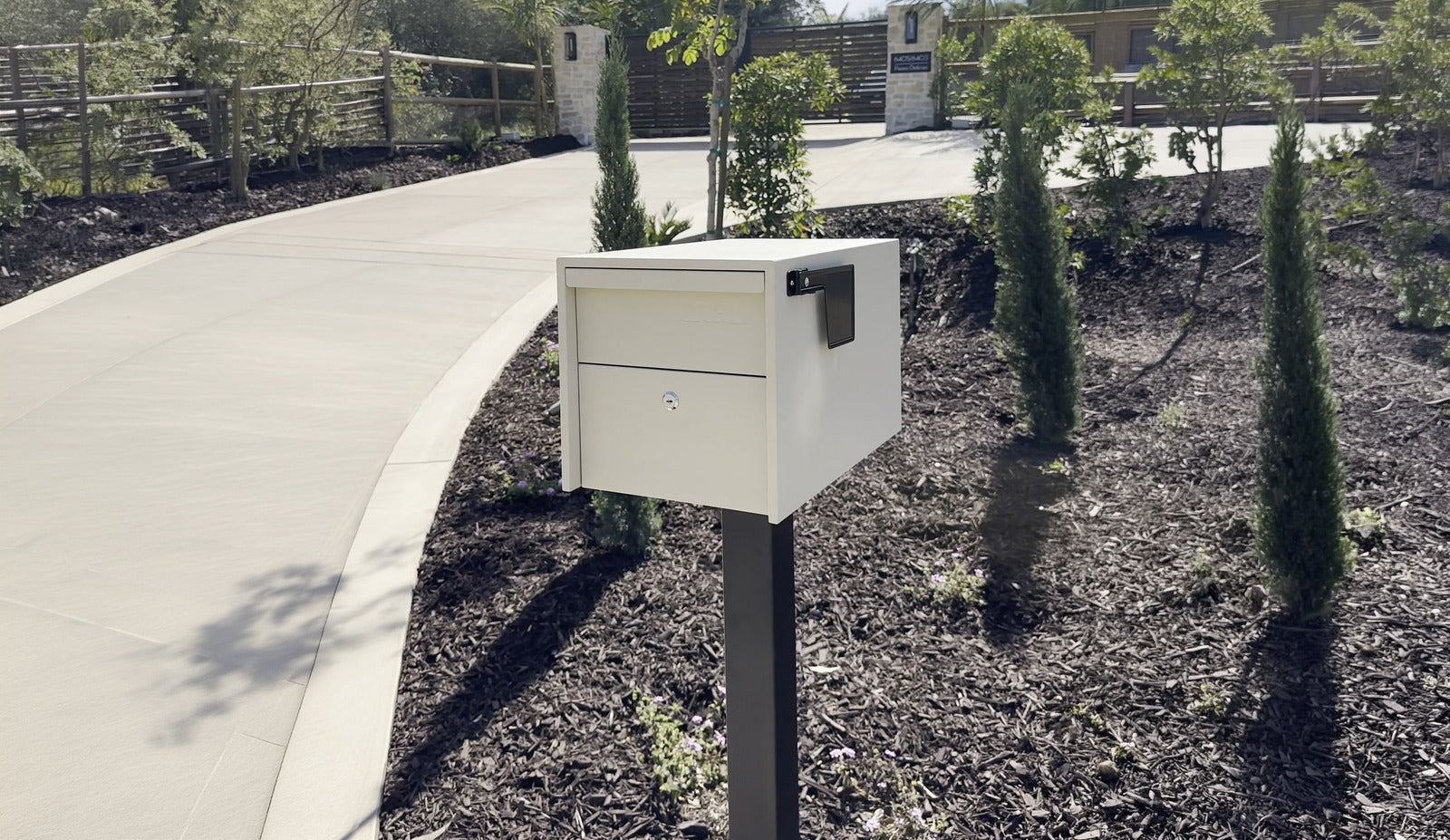 Adoorn Locking Post Mount Mailbox in Sandstone at the curb of a real home with a curving driveway, the calm prevention answer to mail theft.
