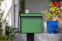 A clean, well-kept Adoorn Post Mount mailbox in forest green on a real porch with flower planters.