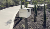 Adoorn Locking Post Mount Mailbox in Sandstone at the curb of a real home with a curving driveway, the calm prevention answer to mail theft.