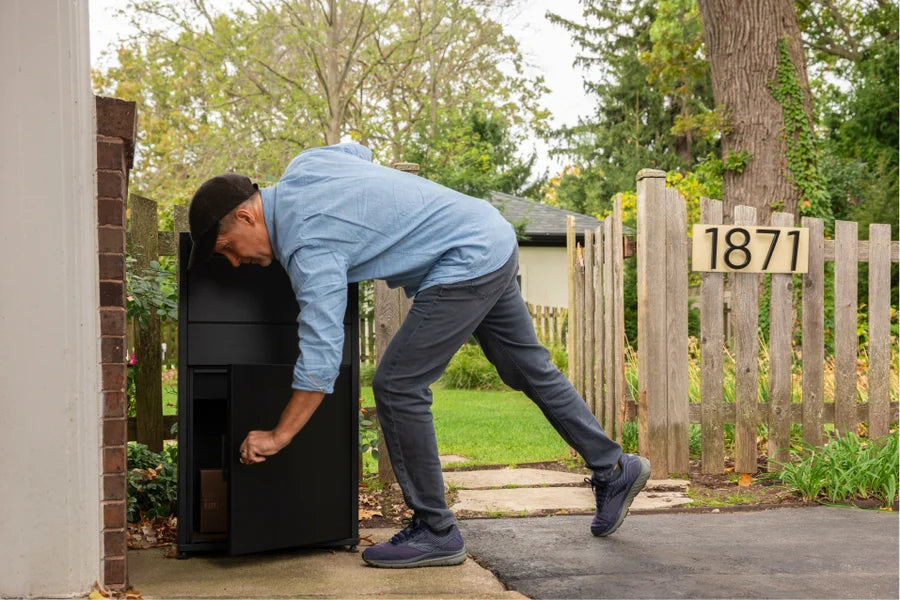 A homeowner retrieving a delivery from a Black package delivery box beside house numbers
