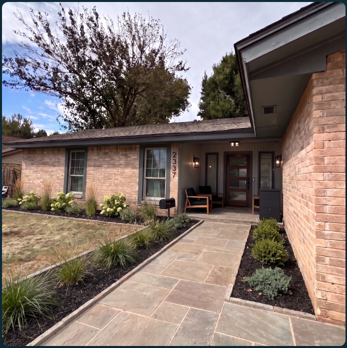 After: the brick home with a stone walkway, planted borders, warm entry lighting, wood seating, mailbox and package box.