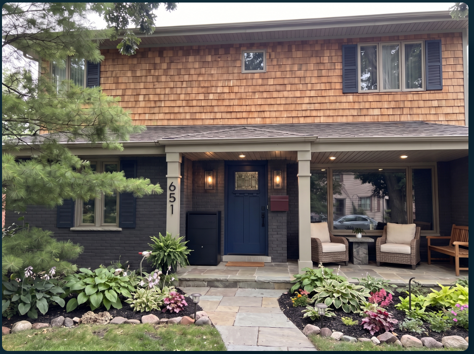 After: the home with wood shingles, dark painted brick, a navy front door, deep-red mailbox, warm lanterns, refreshed seating and a stone path with planted borders.