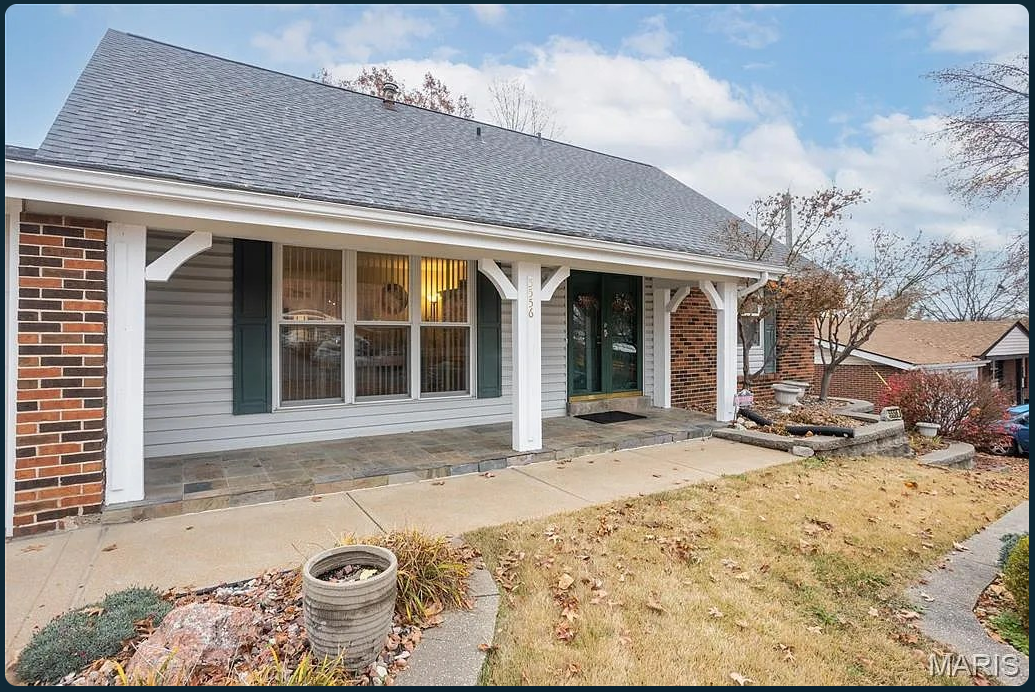 Before: a brick and gray-sided home with an empty covered porch, concrete walk and sparse garden beds.