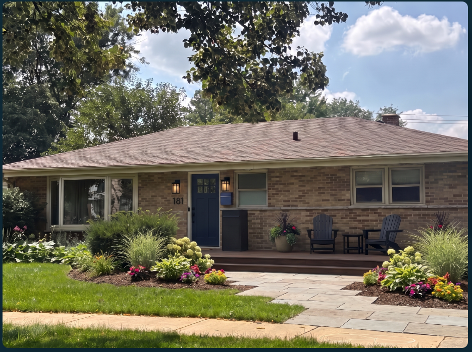 After: the brick ranch with a navy door, warm lanterns, mailbox and package box, a wood porch with dark chairs, stone path and refreshed planting beds.