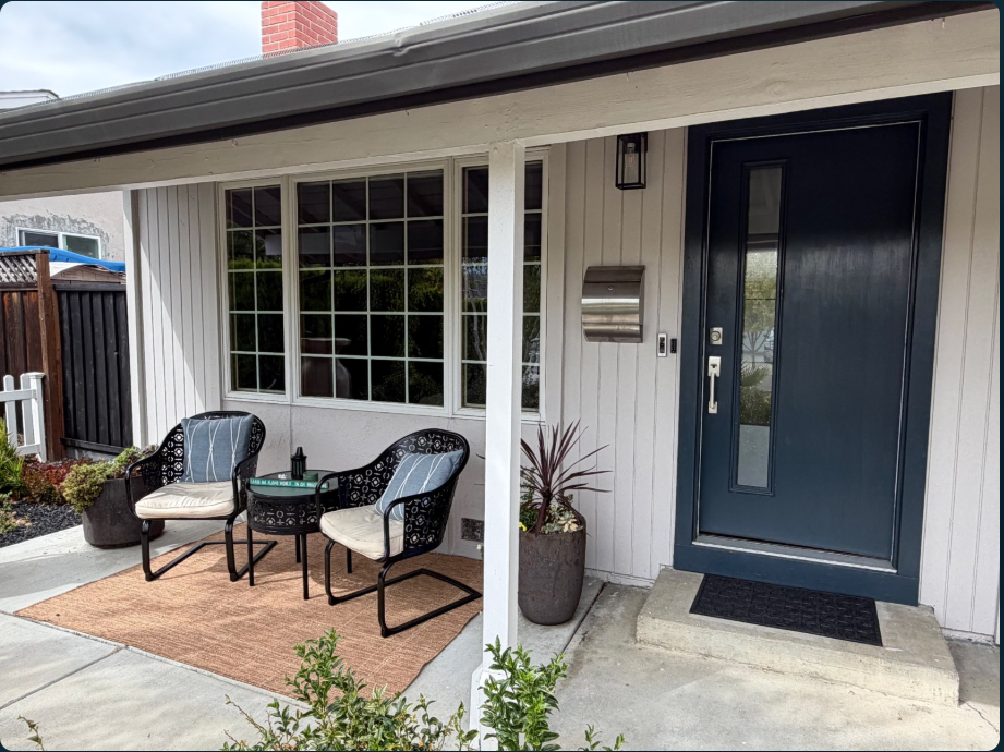 Before: a covered porch with two black chairs, a small round table, a metal mailbox and a dark front door beside a concrete landing.
