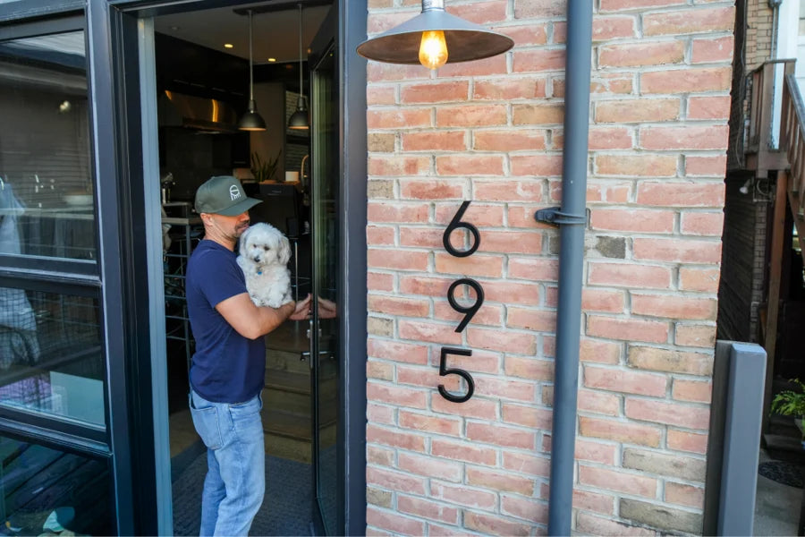 A man and his dog at the door beside large 6-inch house numbers on brick | Adoorn